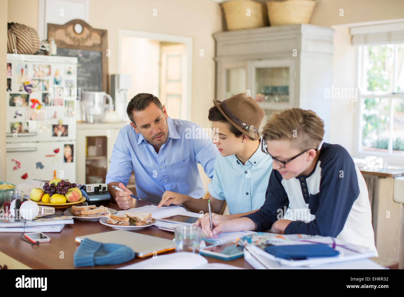 Mid adult man helping teenage boys with their homework at table Stock Photo