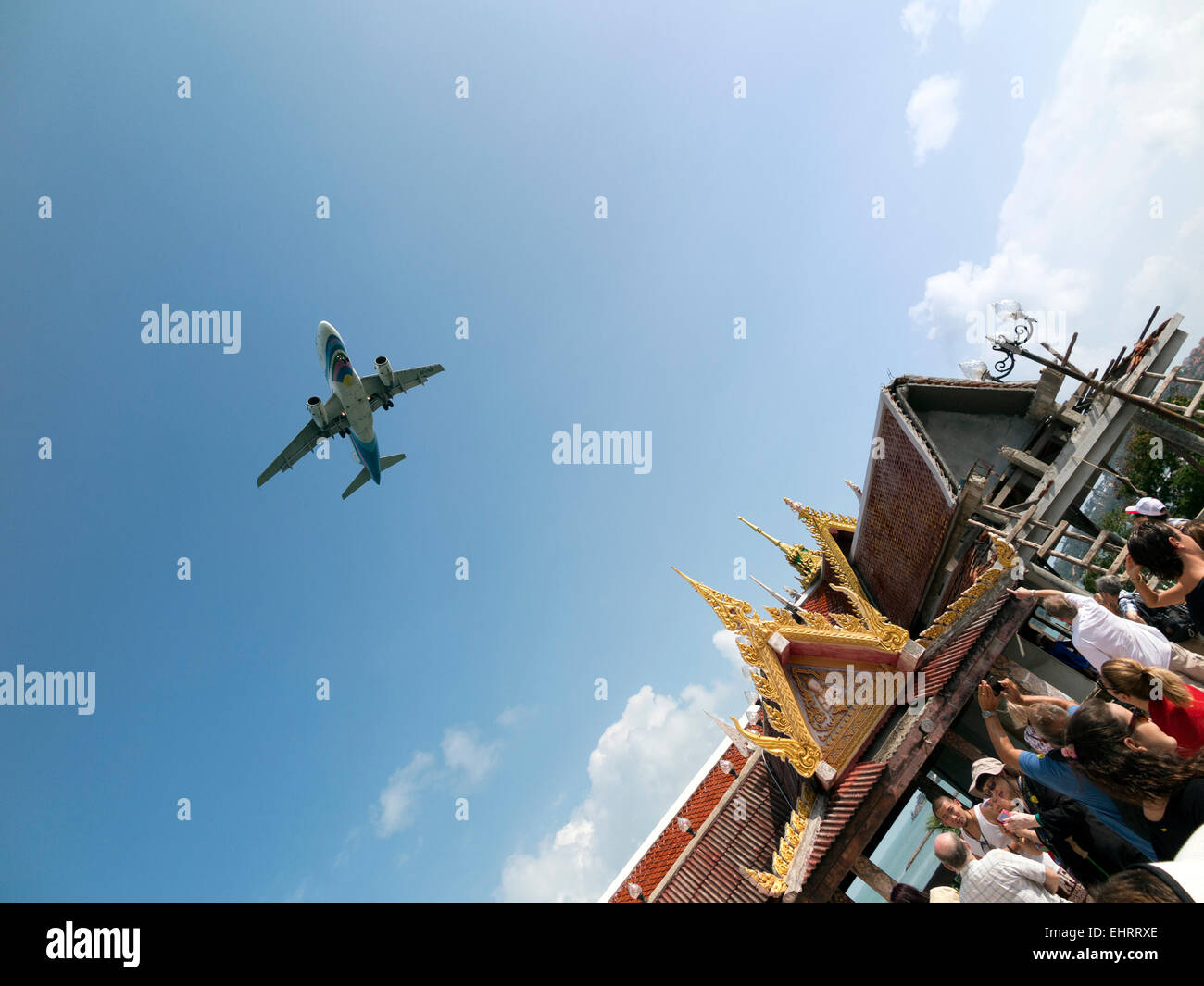 Visitors to the Wat Phrayai Temple in Ko Samui take photographs of a low-flying inward bound aeroplane Stock Photo