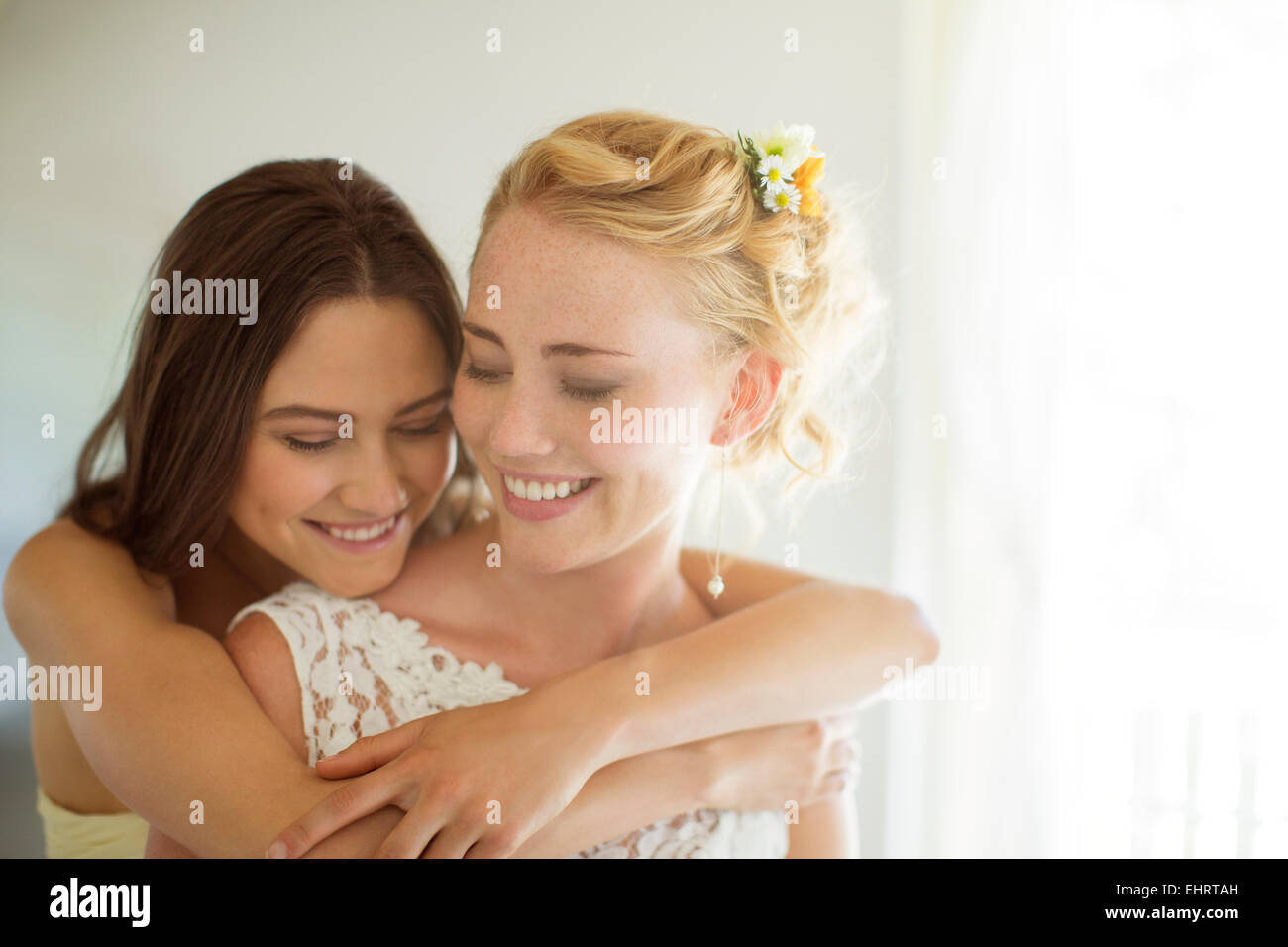 Bridesmaid embracing bride in bedroom Stock Photo