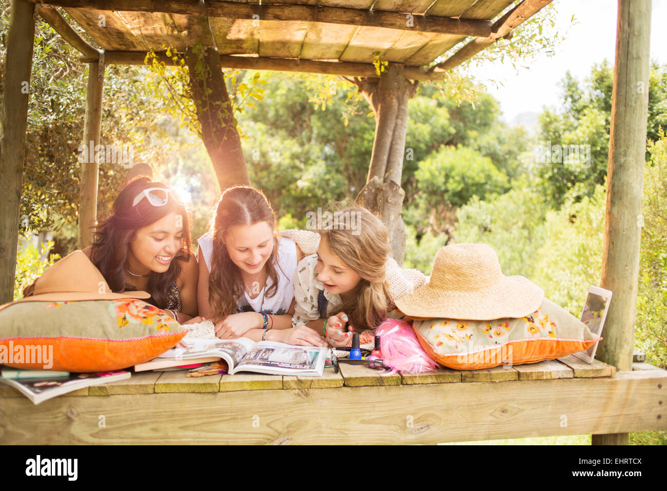 Three teenage girls reading magazine while lying in tree house in summer Stock Photo