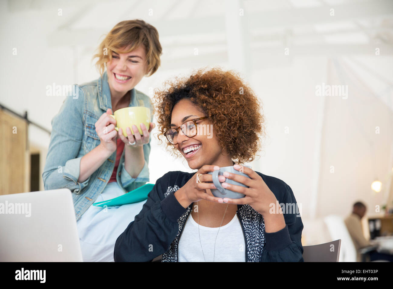 Two office workers talking at desk using laptop Stock Photo - Alamy
