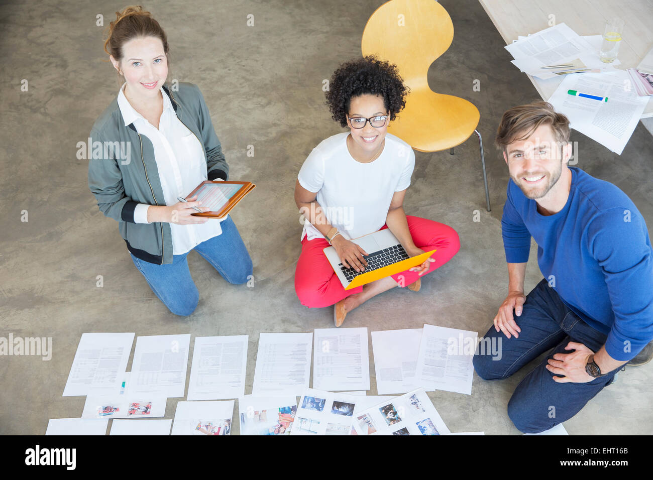 Portrait of three young people sitting on floor and working together in studio Stock Photo