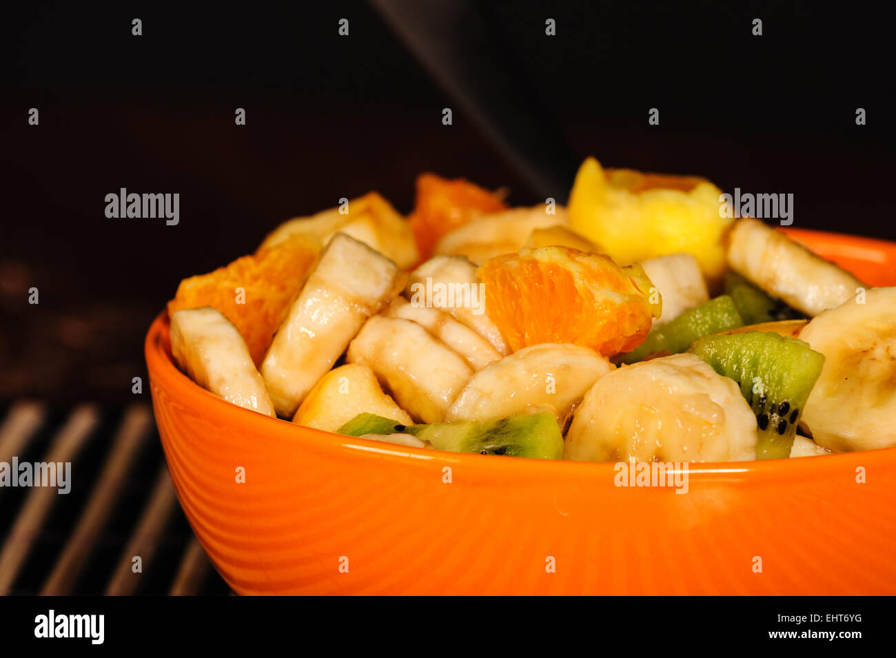 Mixed fruit salad, orange bowl closeup, fresh healthy diet. Still life with black background. Stock Photo