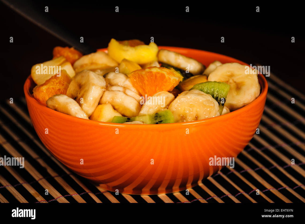 Mixed fruit salad, orange bowl, fresh healthy diet. Still life with black background. Stock Photo