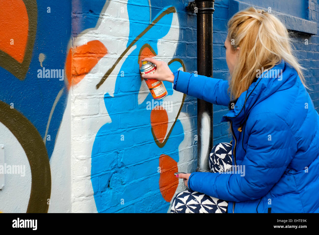 young female street artist spray paints her art onto a wall Stock Photo