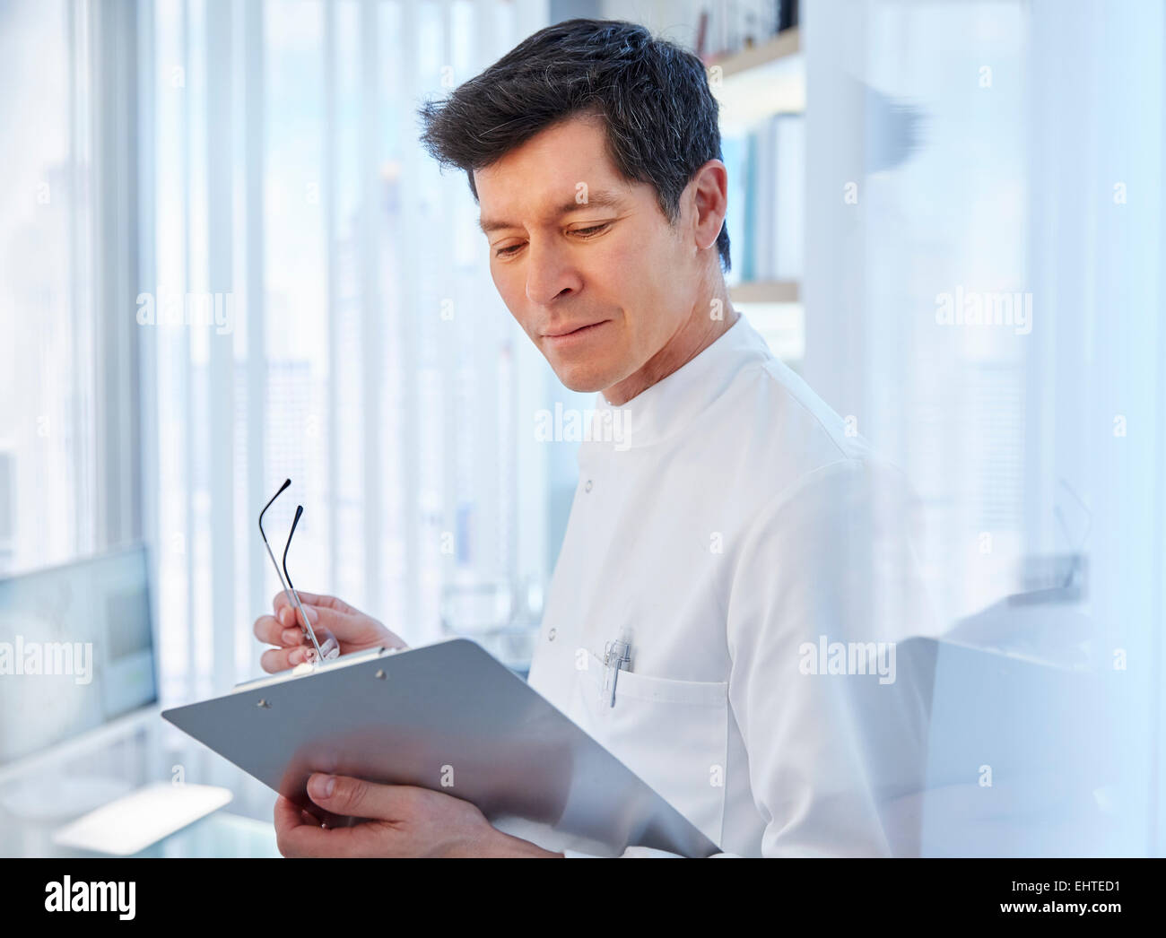 View of man in laboratory holding glasses and chart, looking away Stock Photo