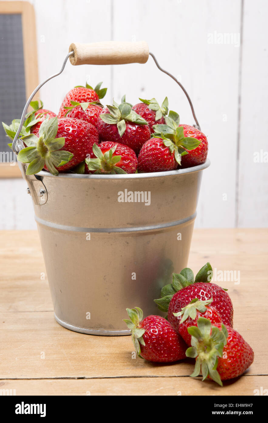 strawberries in a small metallic bucket placed on a old wooden table ...