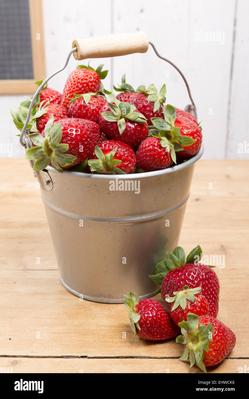 strawberries in a small metallic bucket placed on a old wooden table ...