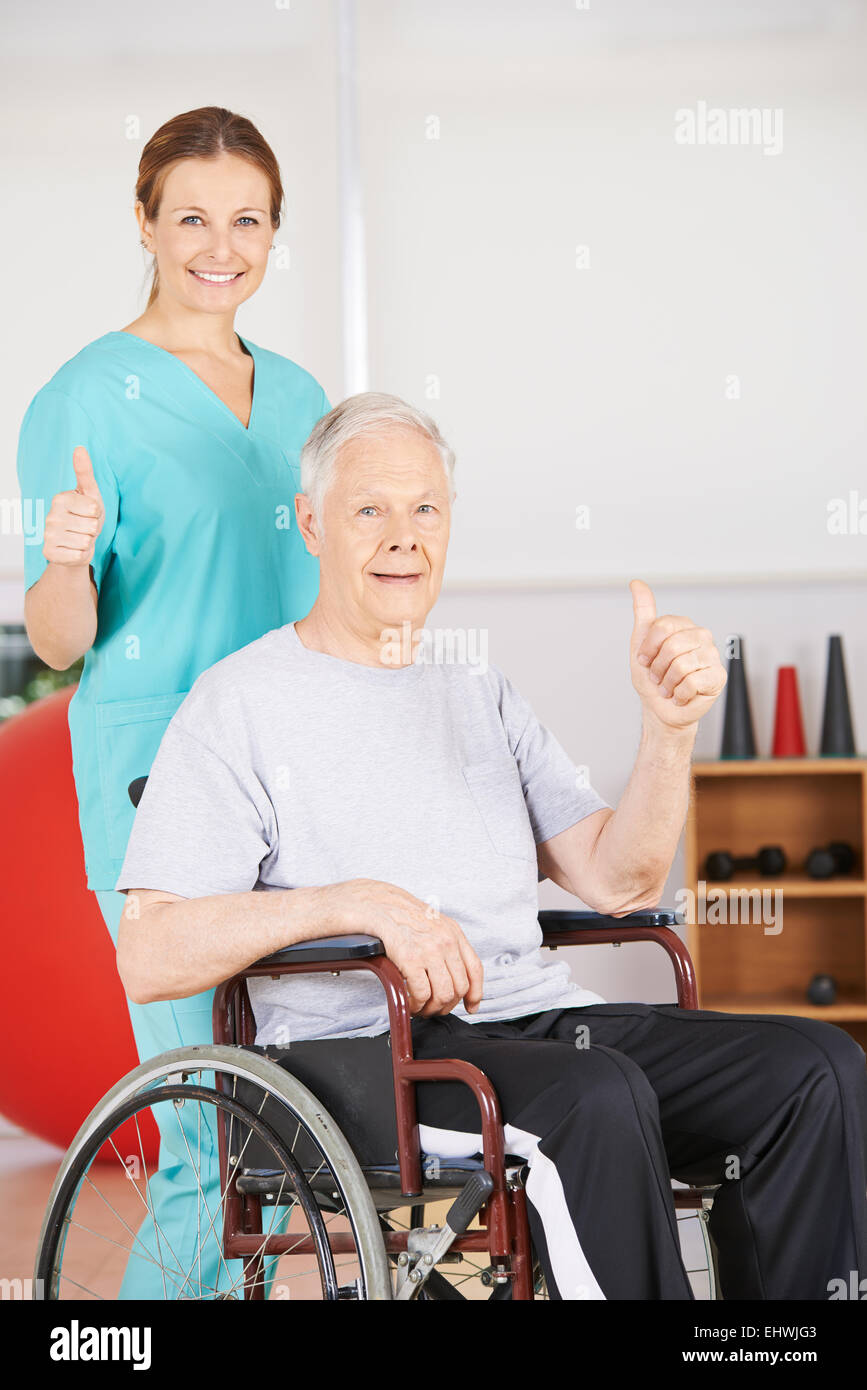 Old senior patient in wheelchair and geriatric nurse holding thumbs up Stock Photo
