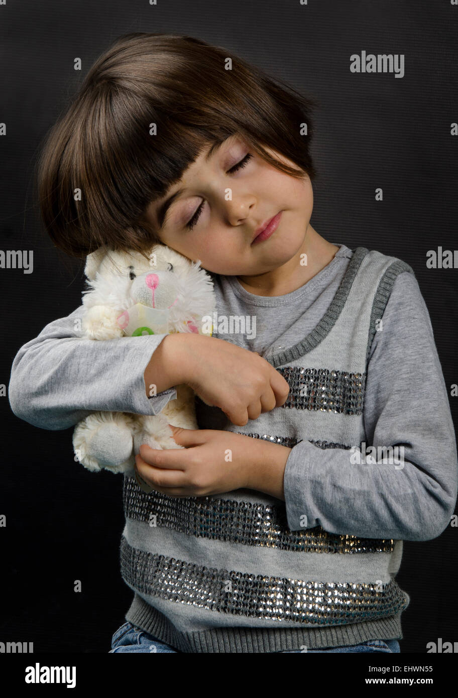 A FOUR YEARS OLD GIRL HOLDING / HUGGING A TOY RABBIT WITH HER EYES