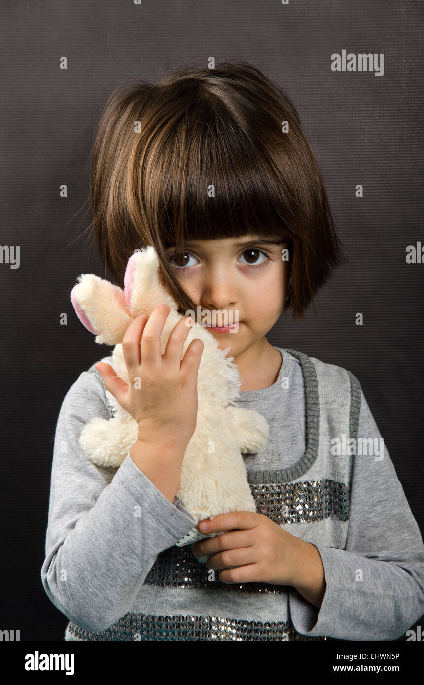 A FOUR YEARS OLD GIRL HOLDING A TOY RABBIT LOOKING PERTURBED Stock