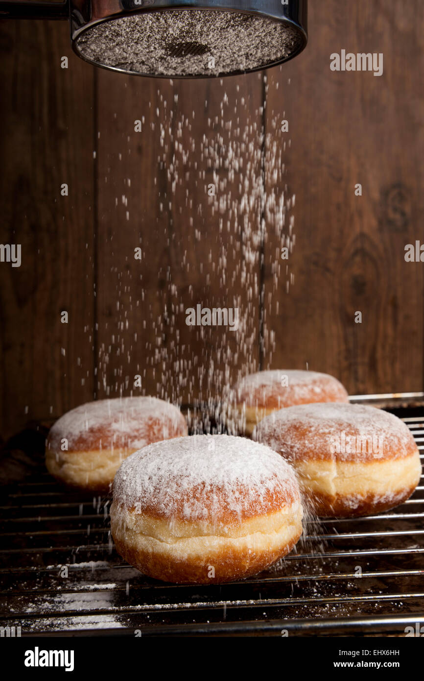 Sprinkling Bismarck doughnuts with icing sugar Stock Photo Alamy