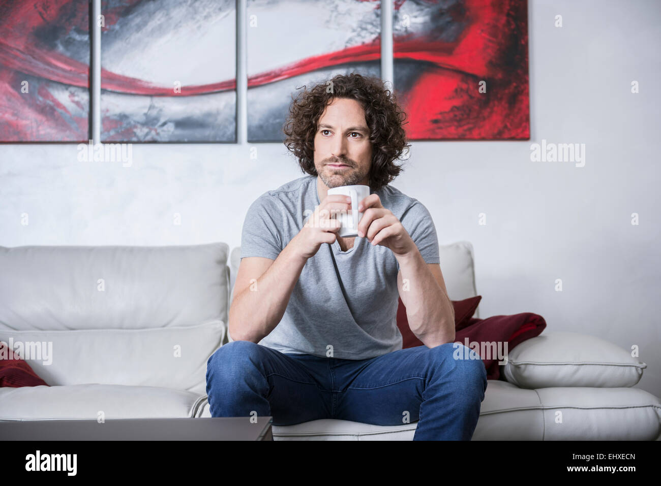 Man sitting on couch and drinking cup of coffee, Munich, Bavaria