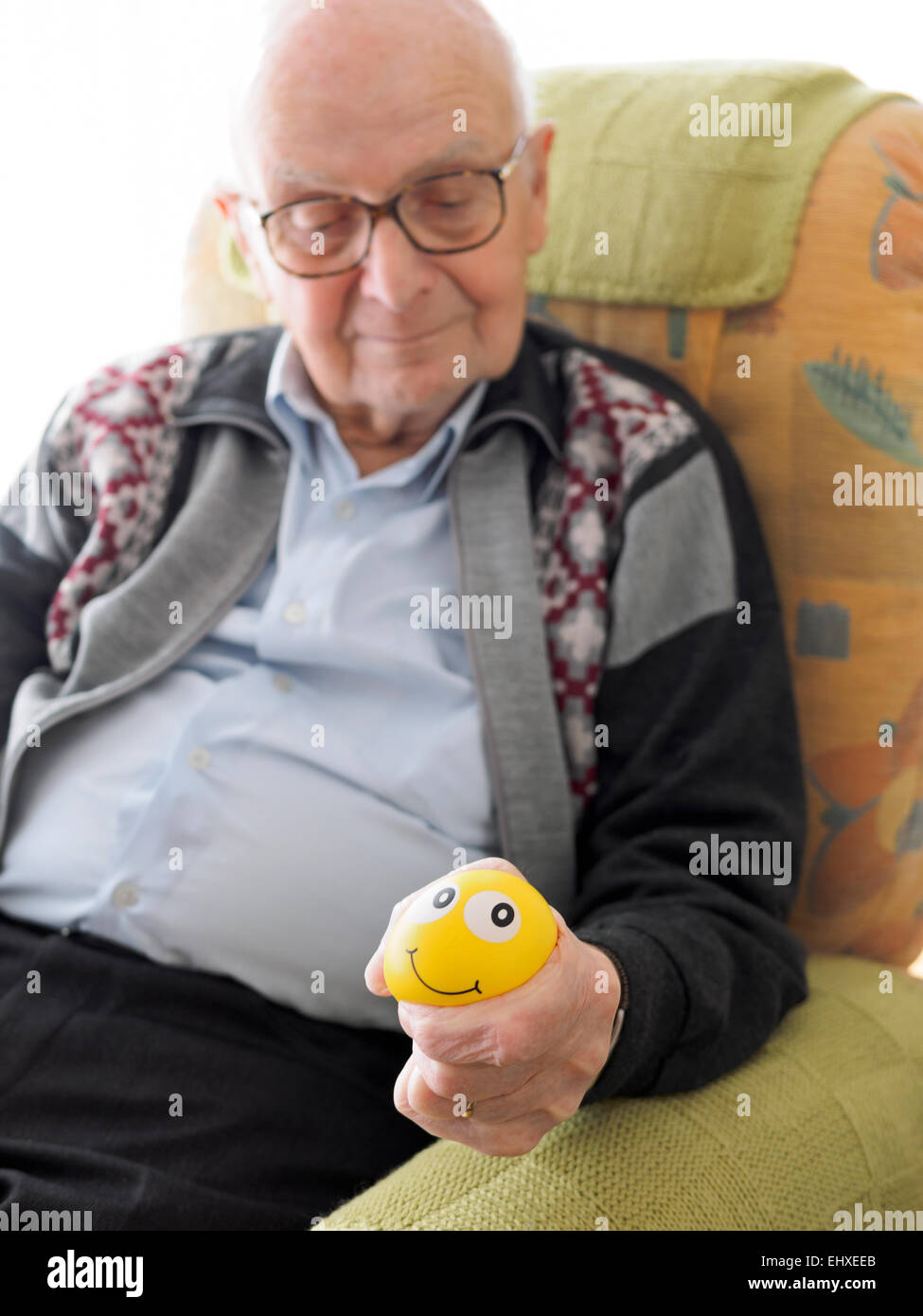 Old man in armchair squeezing stress ball Stock Photo