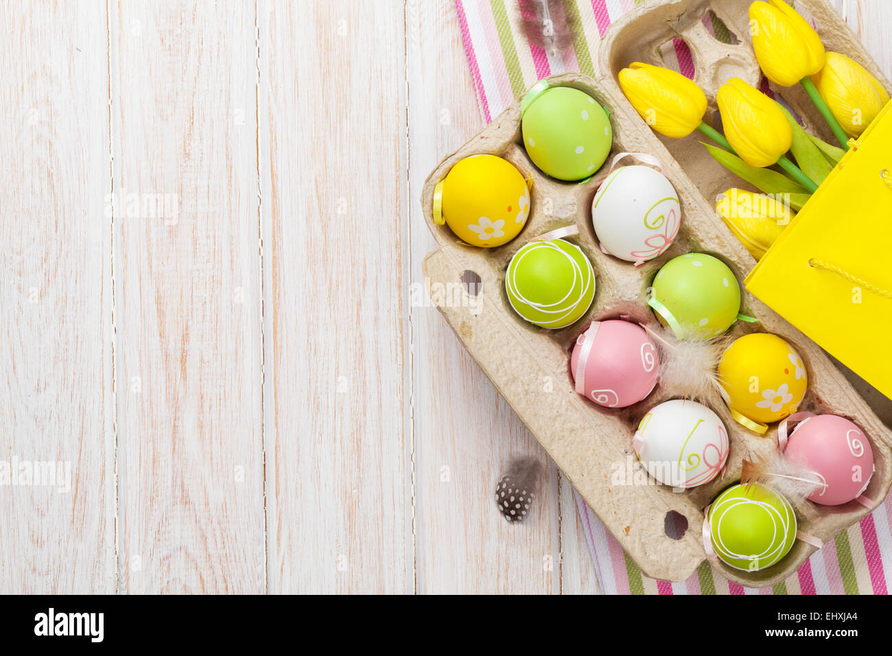 Easter with yellow tulips, colorful eggs and gift bag. Top view with ...