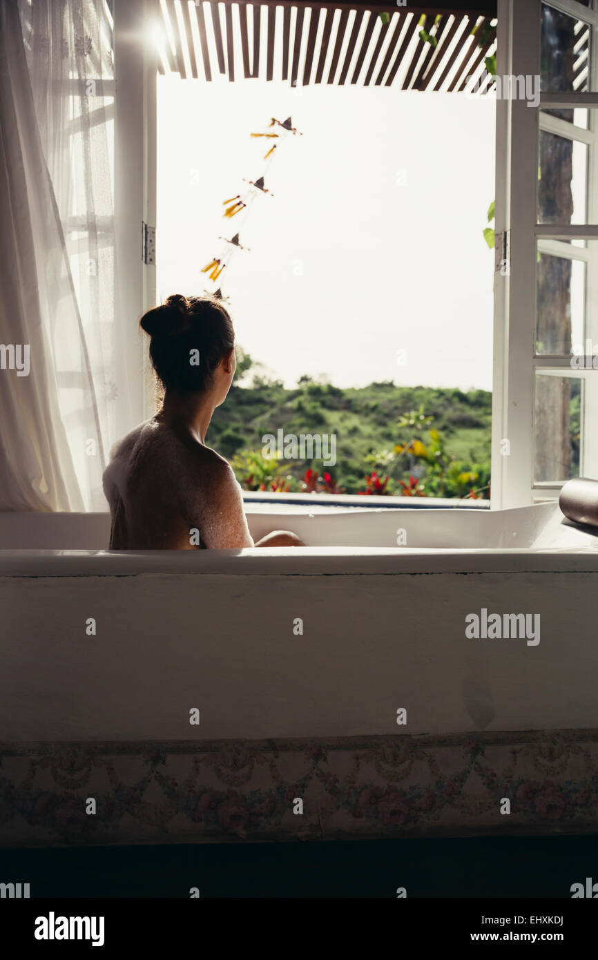 Woman relaxing in bathtub looking out of open window Stock Photo