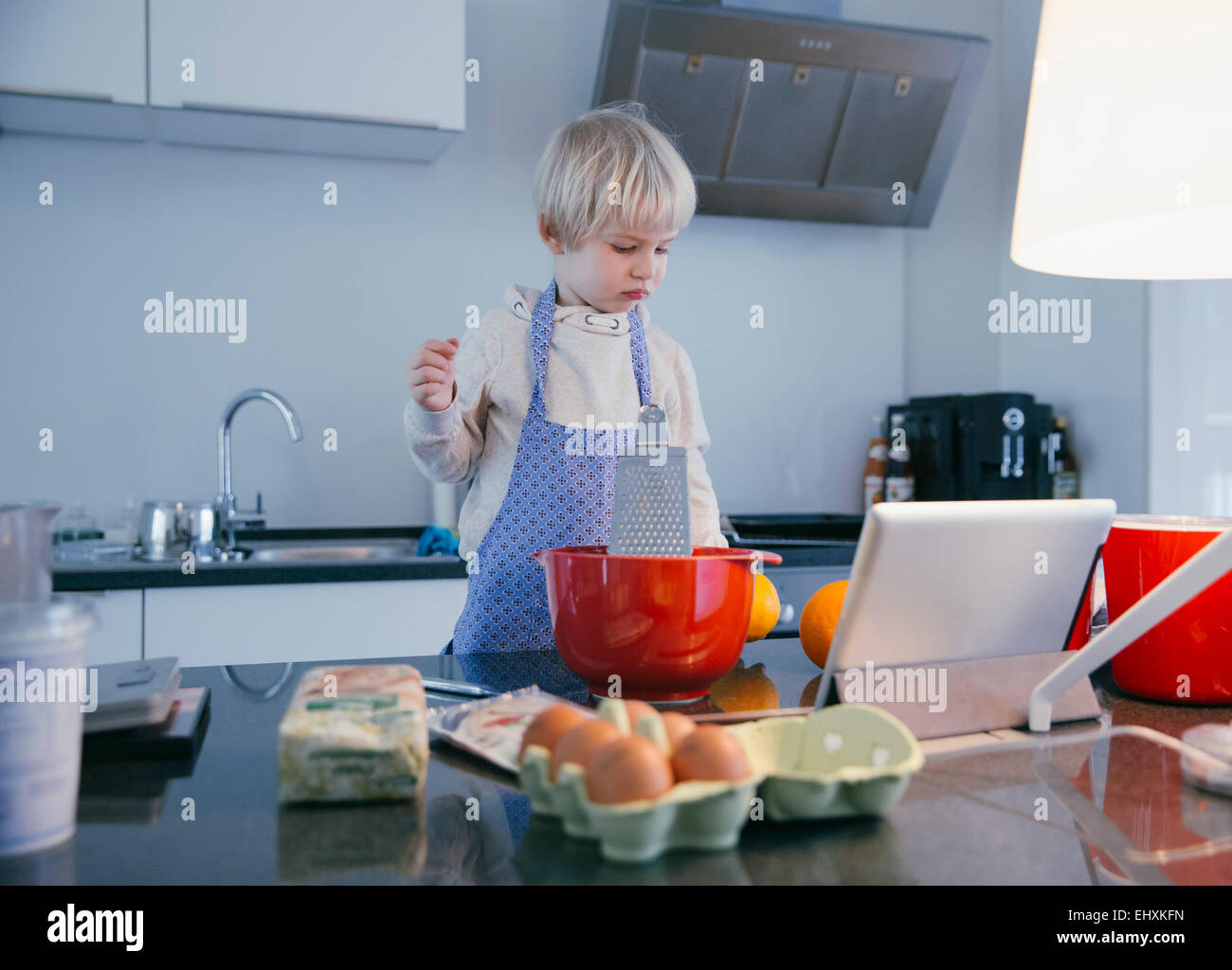 Little boy standing in the kitchen baking with help of digital tablet Stock Photo