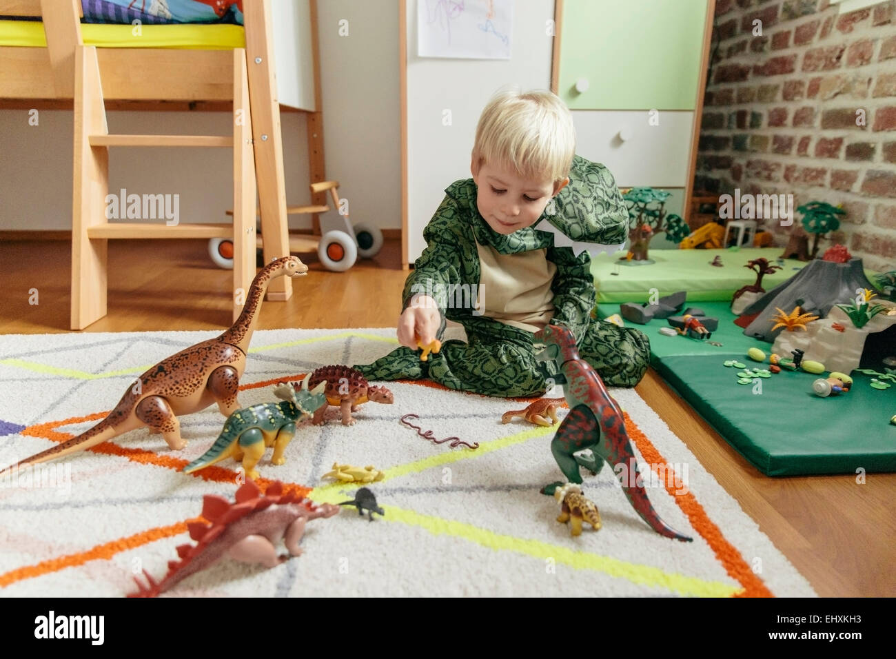 Little boy wearing dinosaur costume playing with toy dinosaurs Stock
