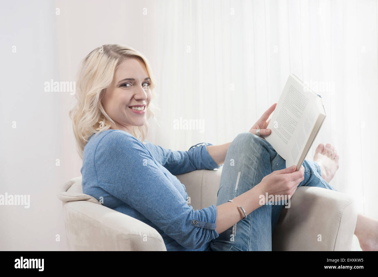 Young blond woman sitting chair reading book Stock Photo - Alamy