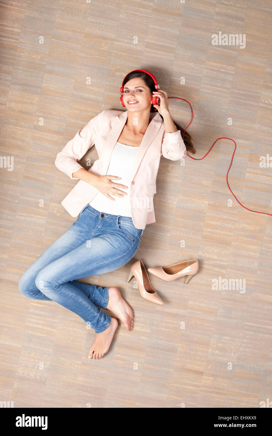 Young woman lying on floor listening to music Stock Photo - Alamy