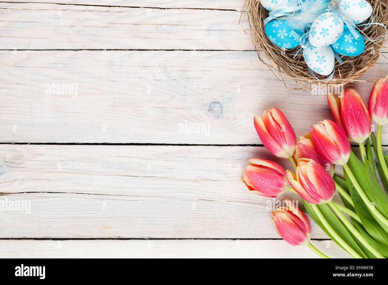 Colorful tulips and easter eggs in nest on wooden table. Top view with ...