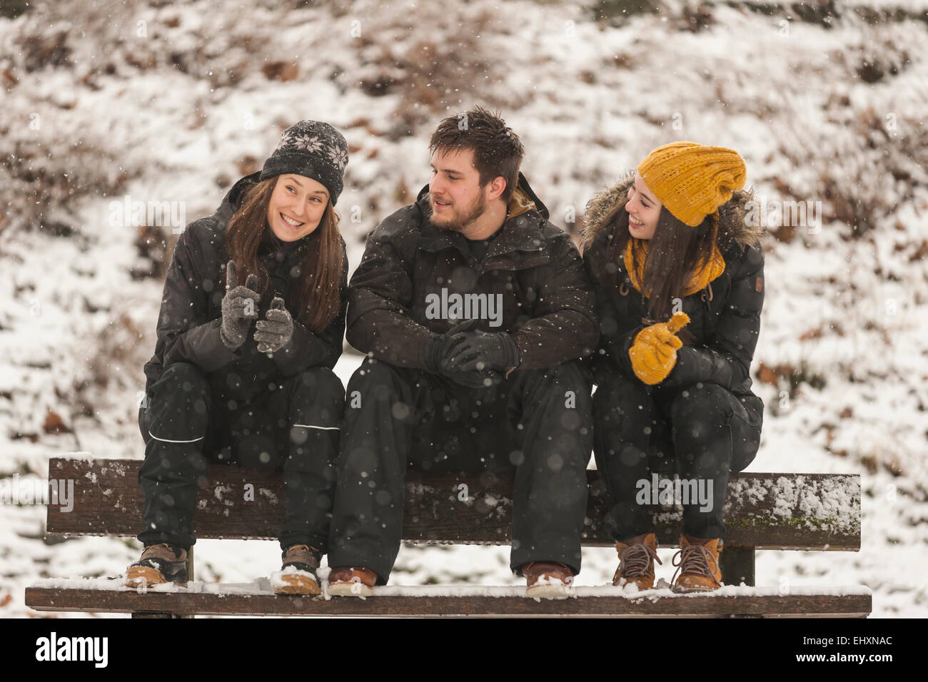 Three friends stting in  row on wooden bench in winter Stock Photo