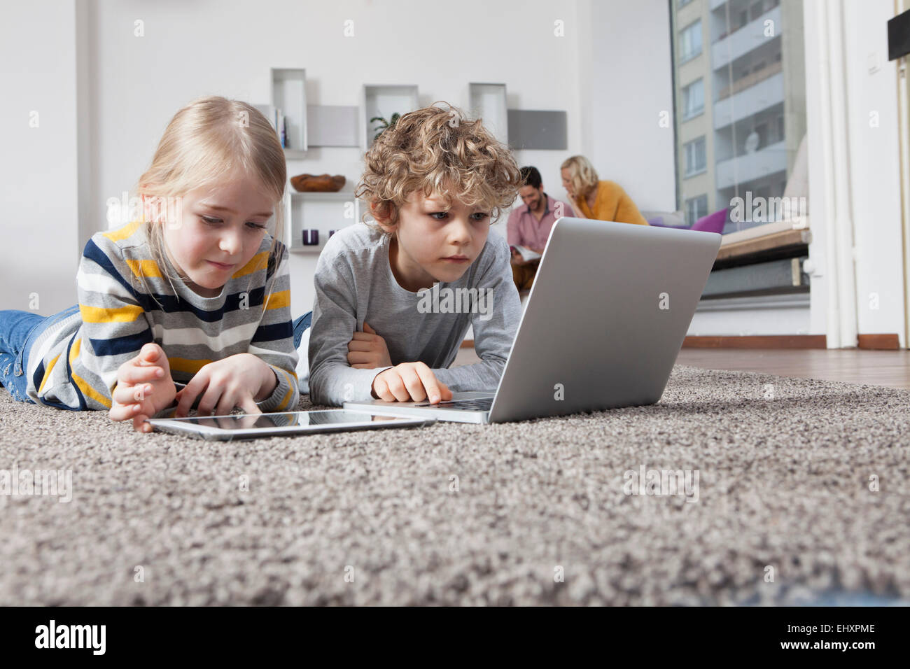 Brother and sister lying on floor using laptop and digital tablet Stock ...