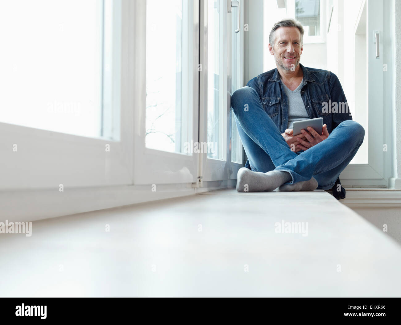 Germany, Cologne, Mature man sitting at window using digital tablet Stock Photo