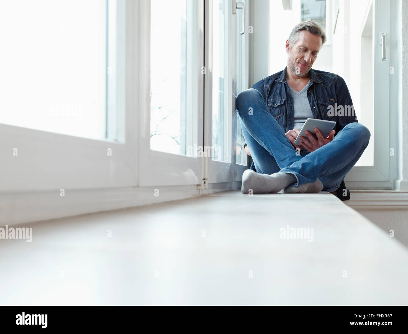 Germany, Cologne, Mature man sitting at window using digital tablet Stock Photo
