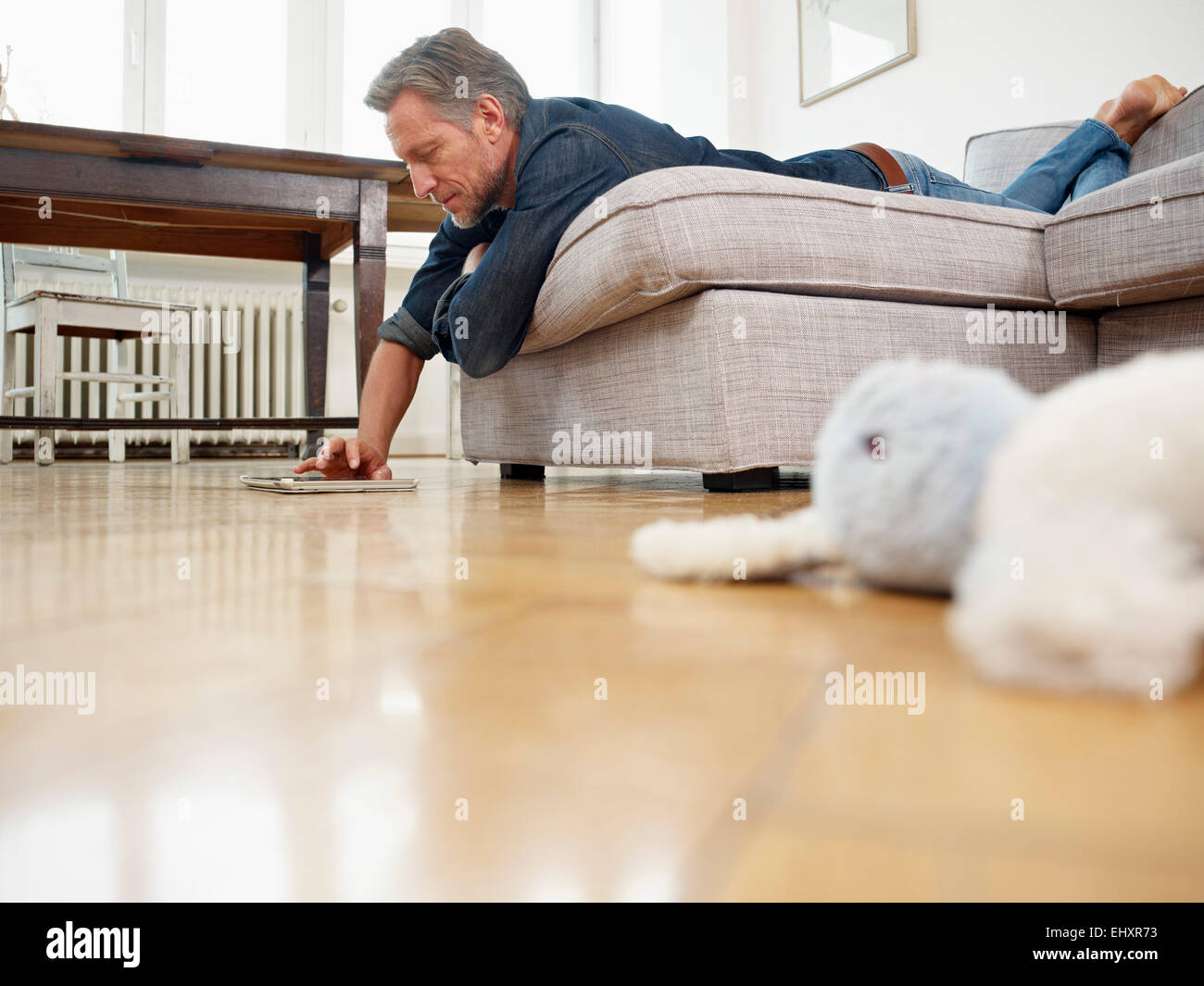 Mature man lying on sofa using digital tablet Stock Photo