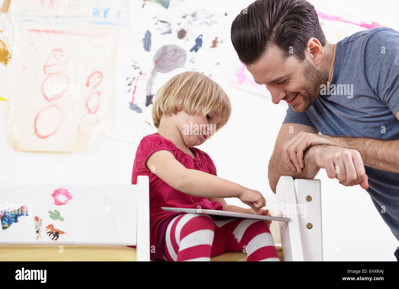 Little girl sitting on bunk bed, drawing on touch pad, father watching Stock Photo