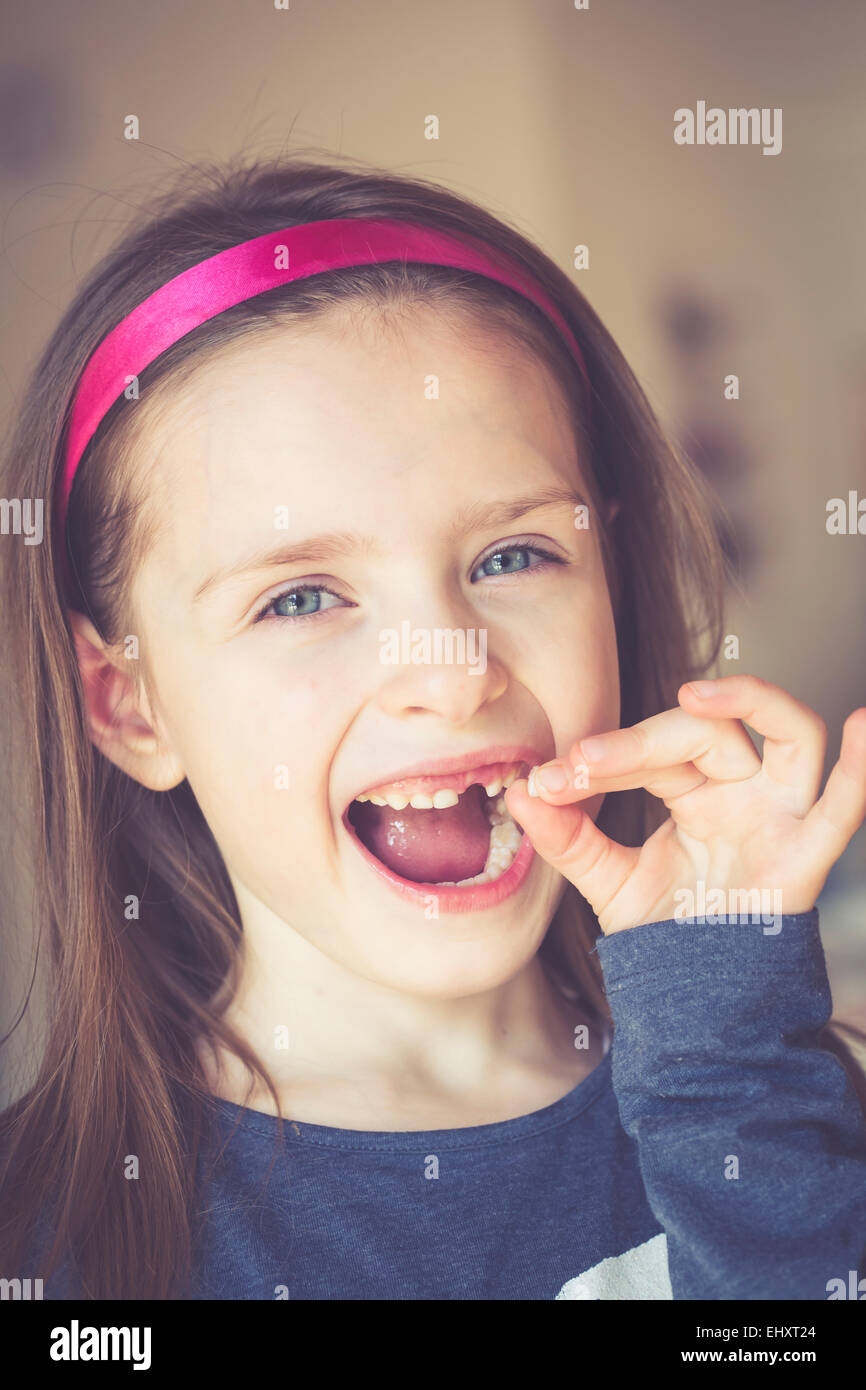 Portrait of smiling little girl with tooth gap holding milk tooth in