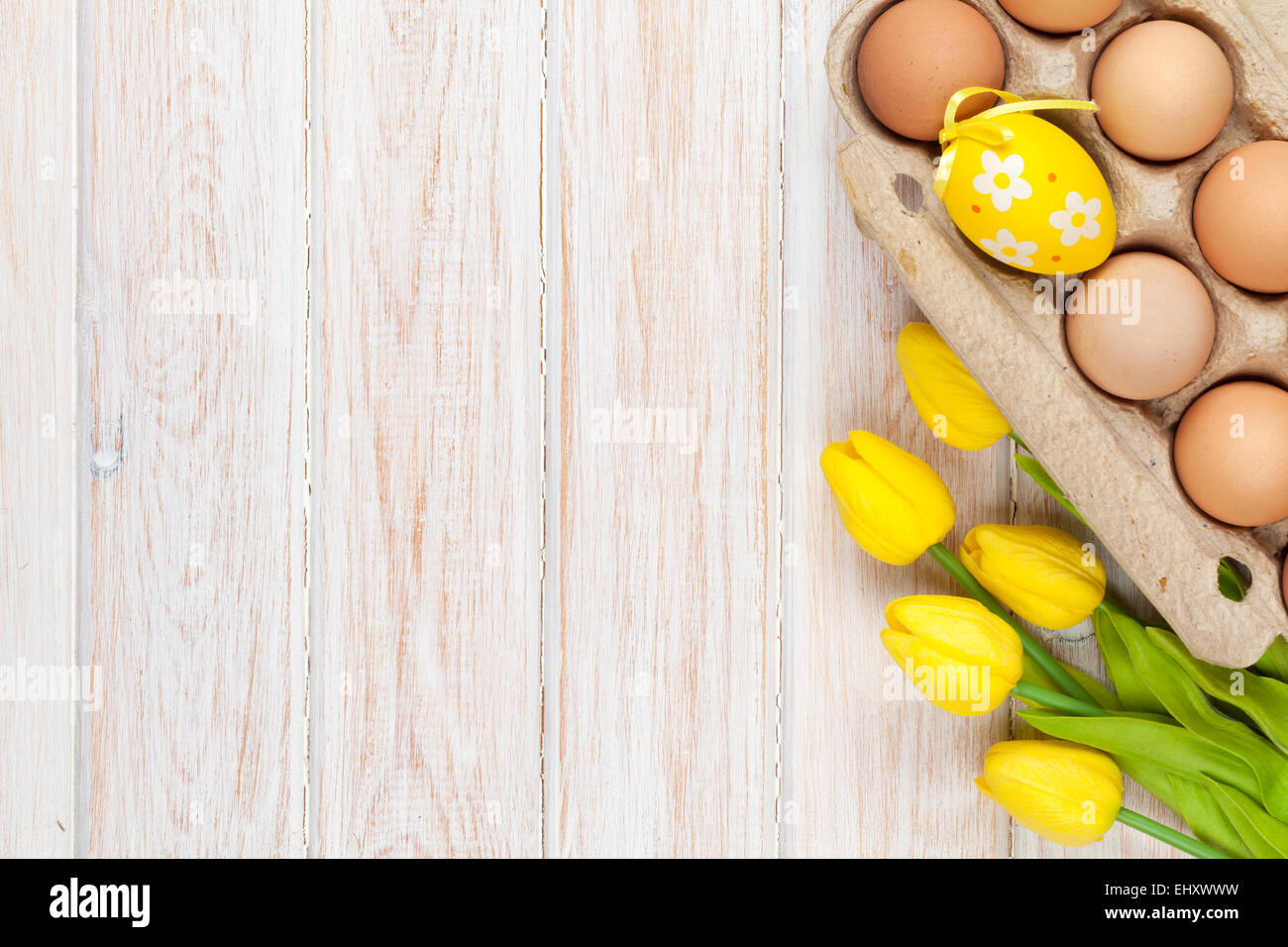 Easter background with eggs and yellow tulips over white wood. Top view ...