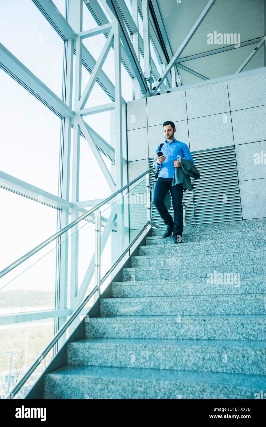 Young businessman walking on stairs looking on cell phone Stock Photo ...
