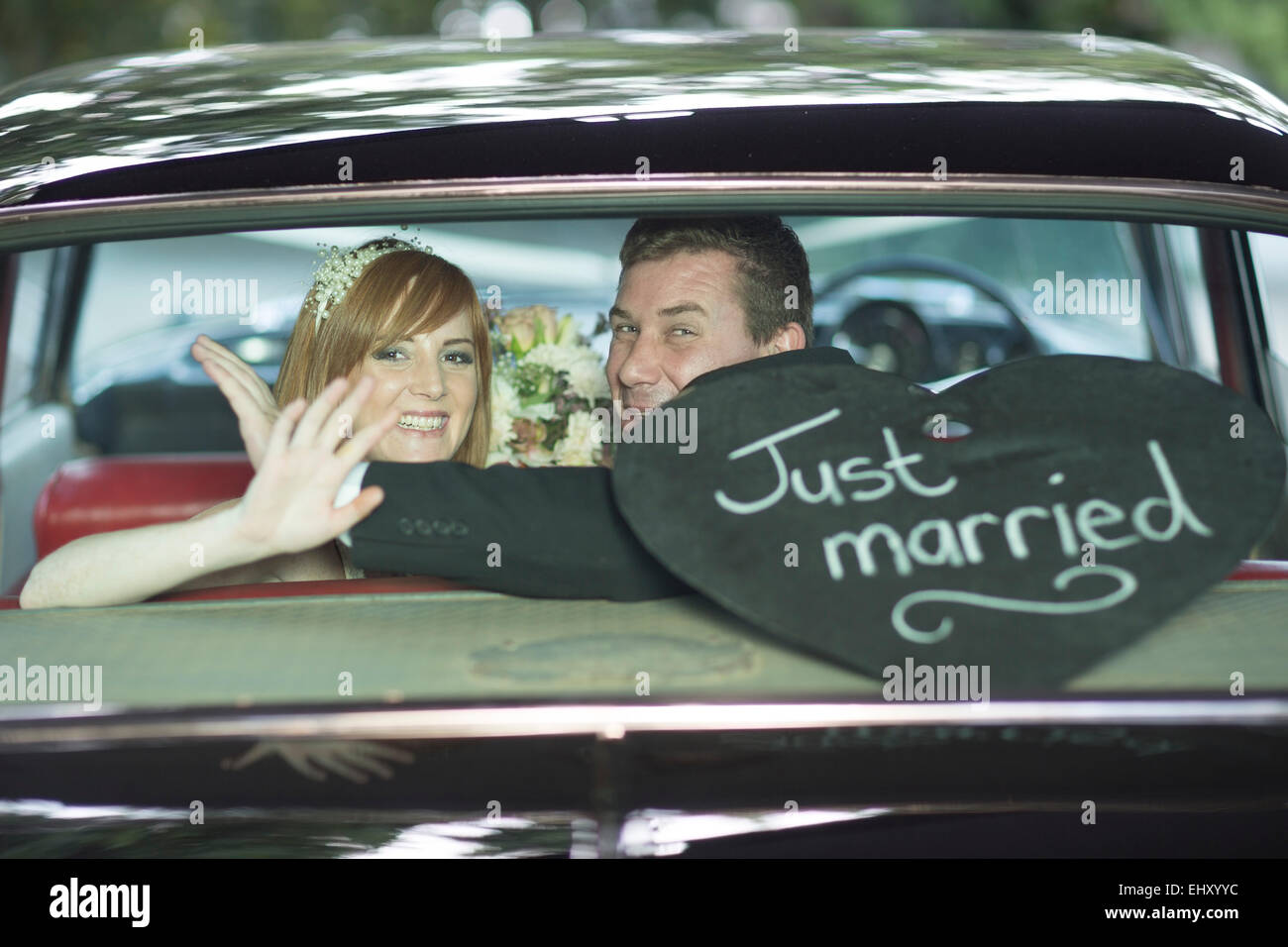 Happy bride and groom waving in car after the wedding Stock Photo - Alamy