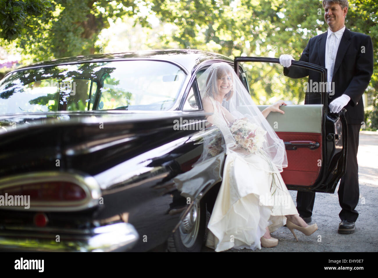 Bride getting out of car before her wedding with driver Stock Photo - Alamy