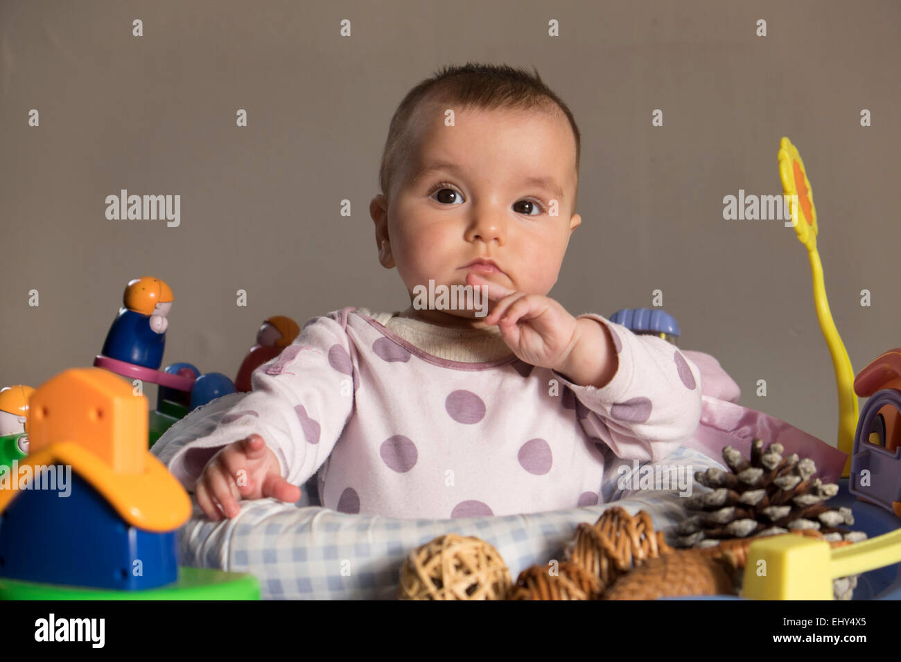 8 month old baby girl, surrounded by toys in baby bouncer Stock Photo