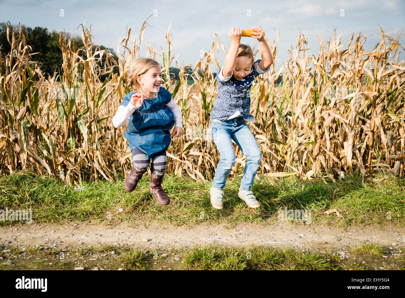 Two girls jumping in front of maize field Stock Photo