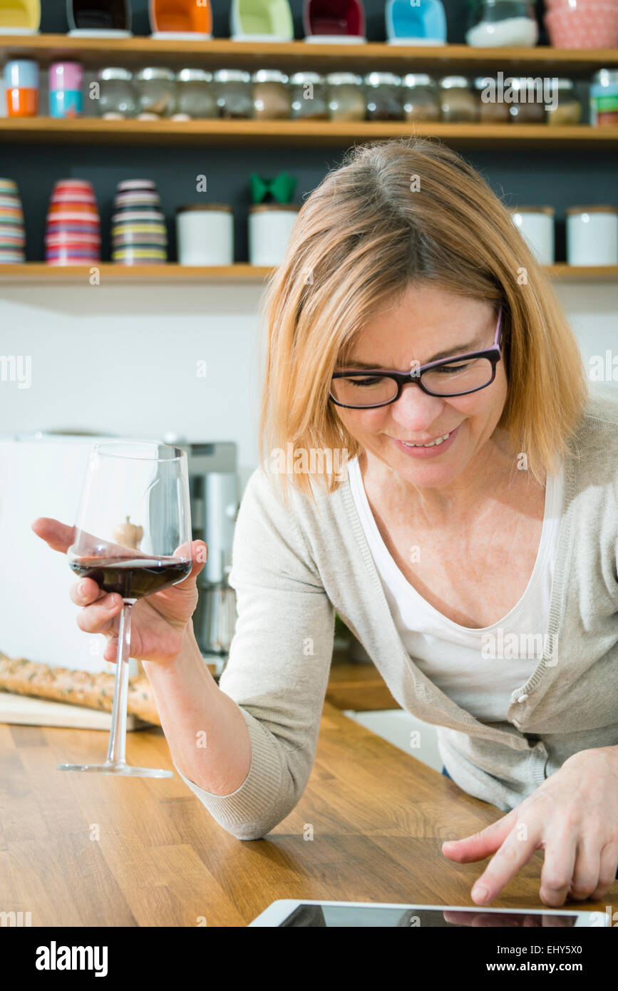 Senior woman holding glass of red wine and using digital tablet Stock Photo