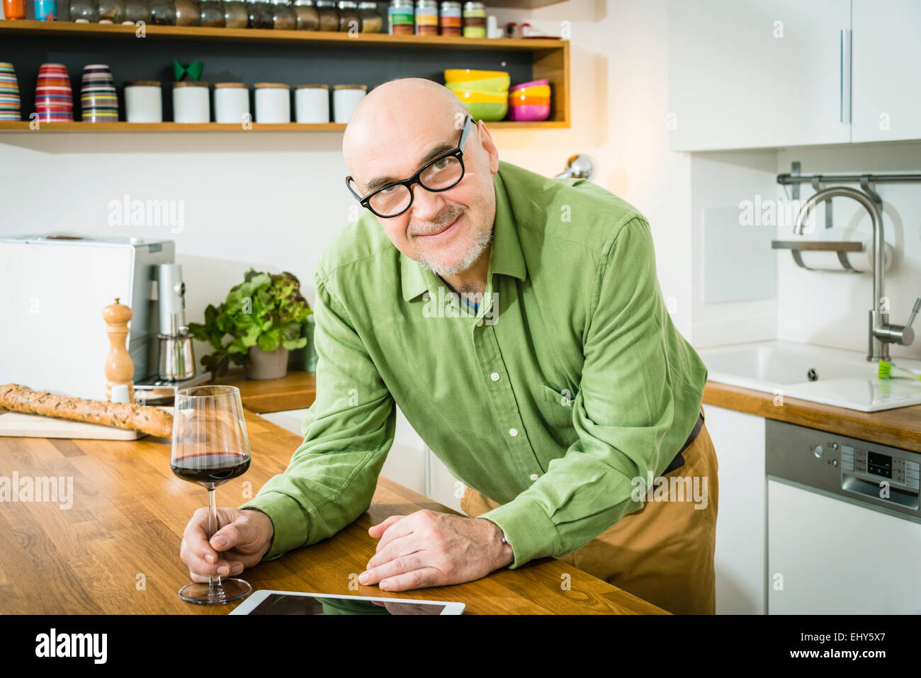 Senior man in kitchen holding glass of red wine, Stock Photo