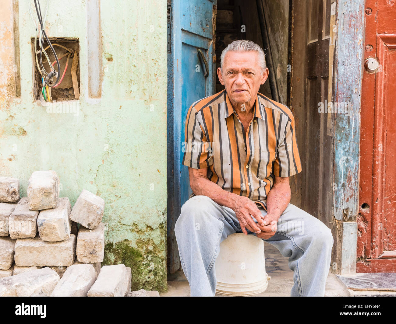 A Hispanic senior citizen rests as he sits on the front stoop of his house in Santiago de Cuba. Stock Photo