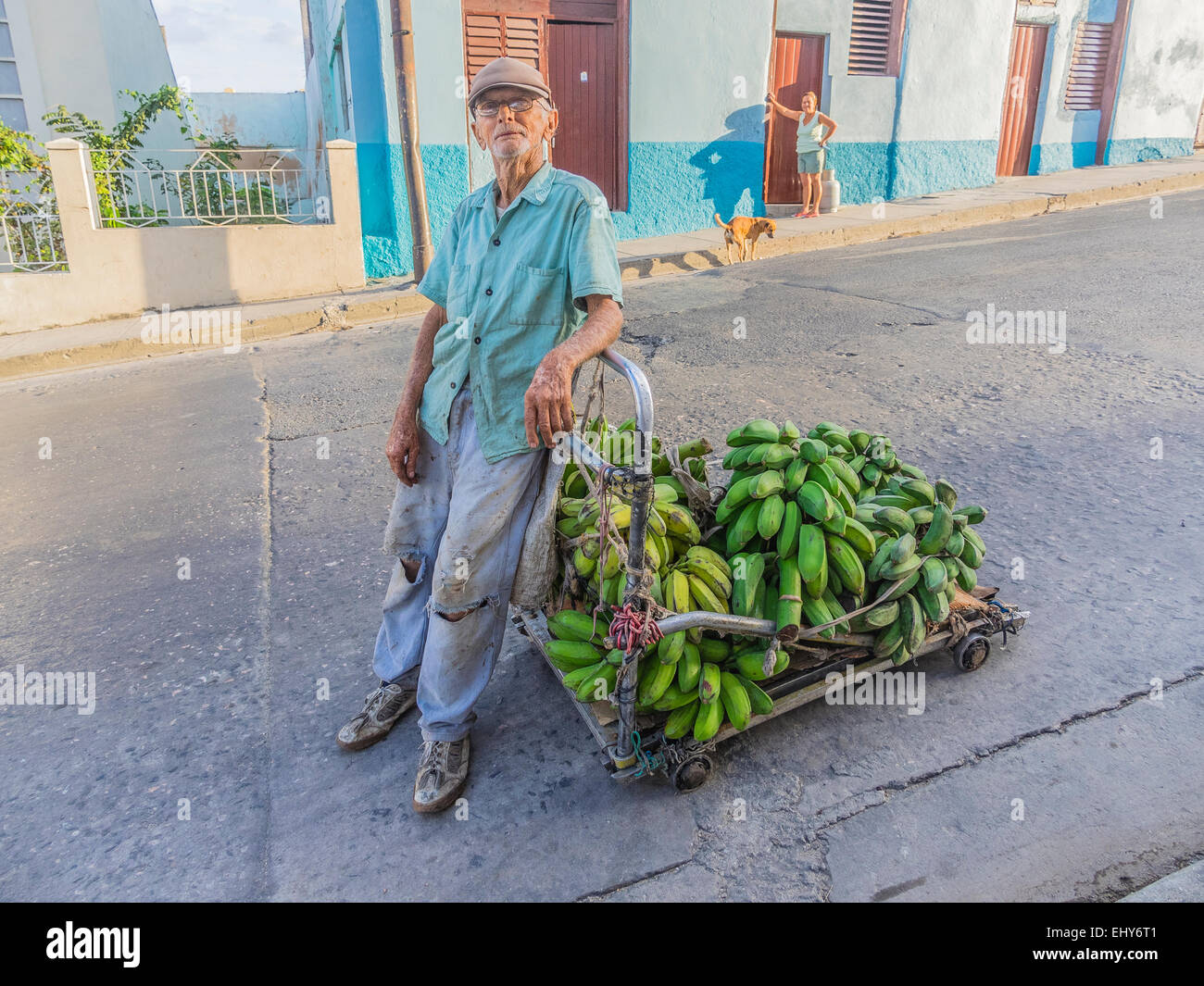 An old Hispanic man pulls his 4-wheeled cart loaded with green plantains through the streets of Santiago de Cuba. Stock Photo