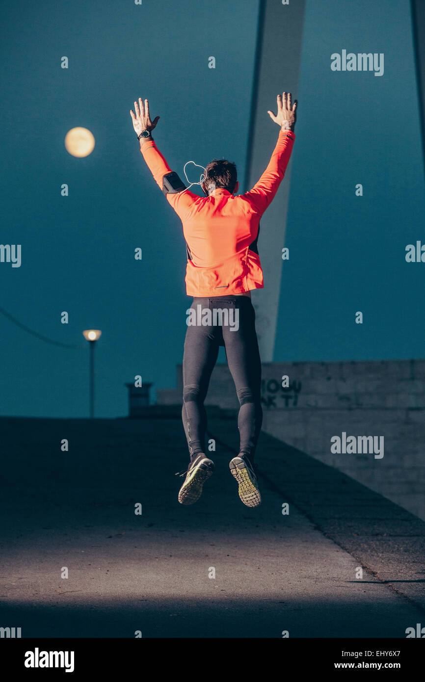 Male runner jumping and warming up against full moon Stock Photo