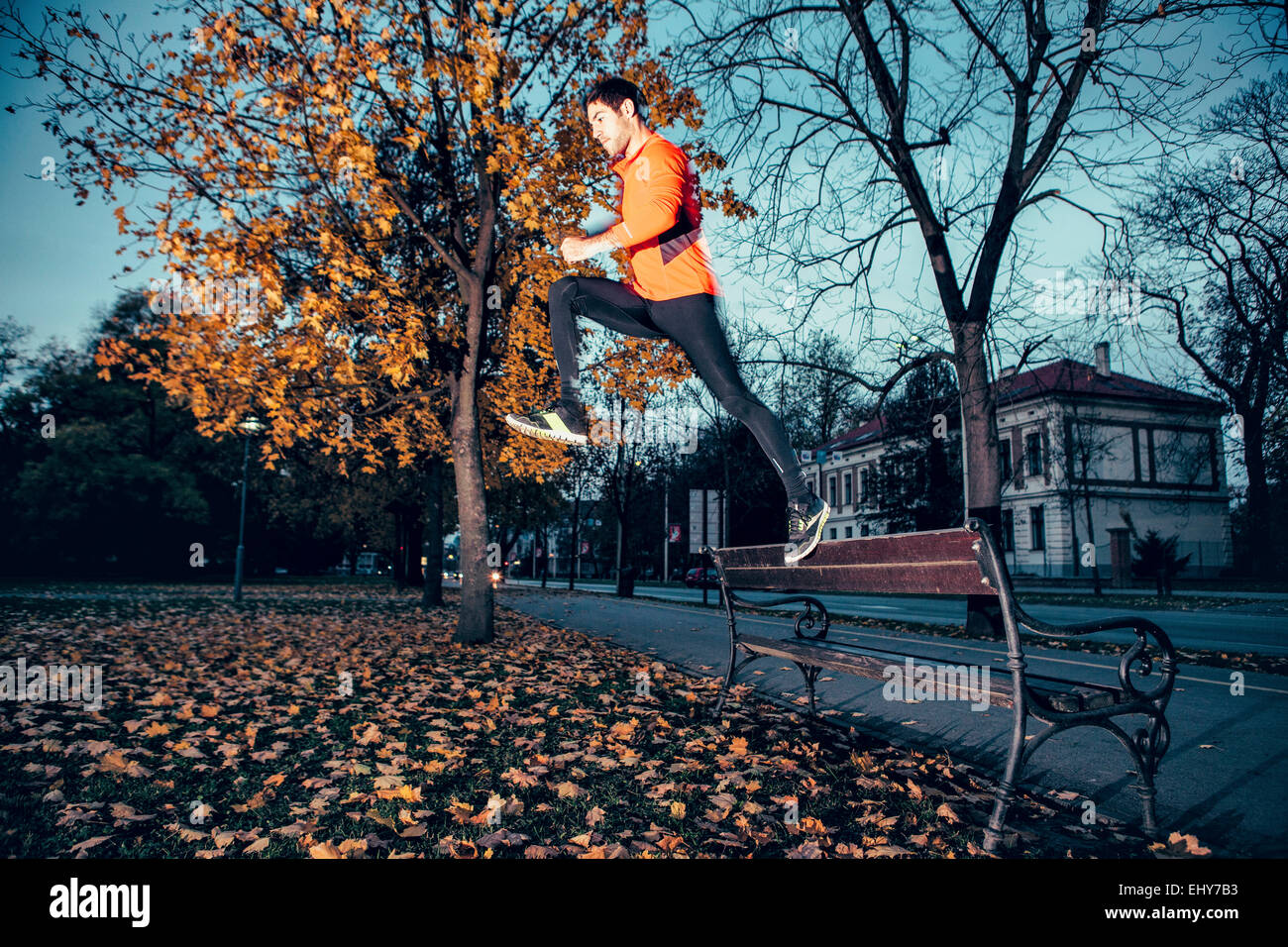 Male runner jumping over bench in park Stock Photo