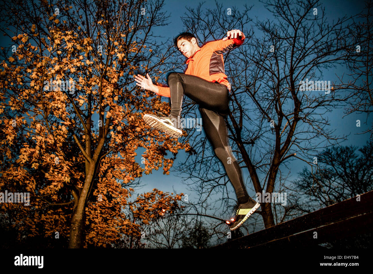 Male runner jumping over bench in park Stock Photo