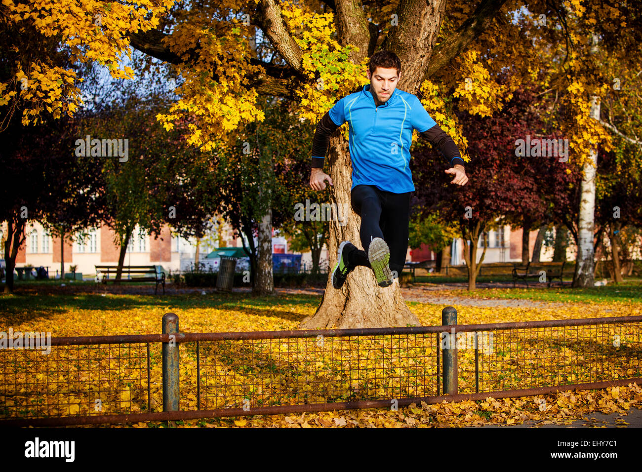 Male runner jumping over fence in autumn park Stock Photo