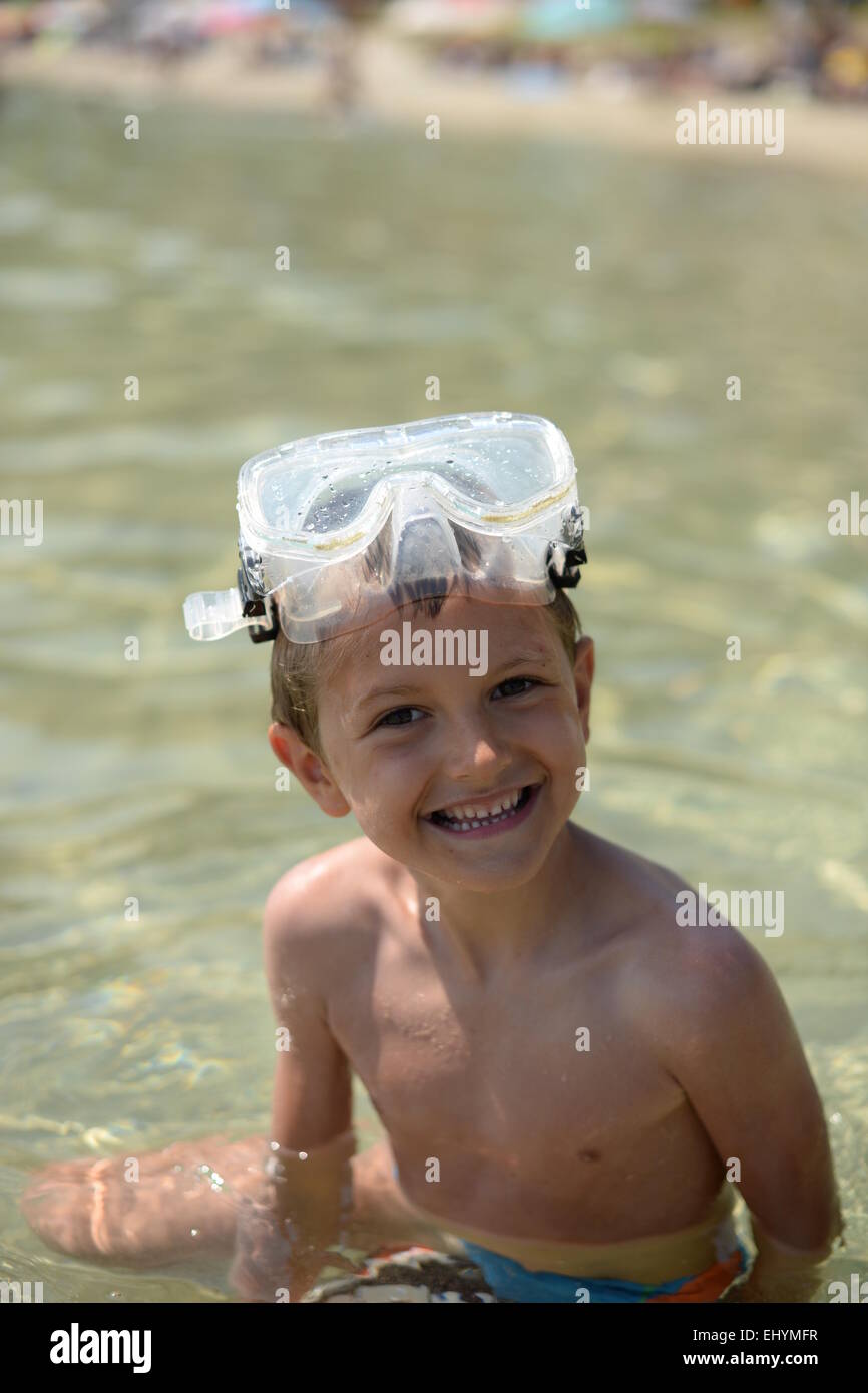 Portrait of a smiling boy sitting in the sea wearing goggles on his head Stock Photo