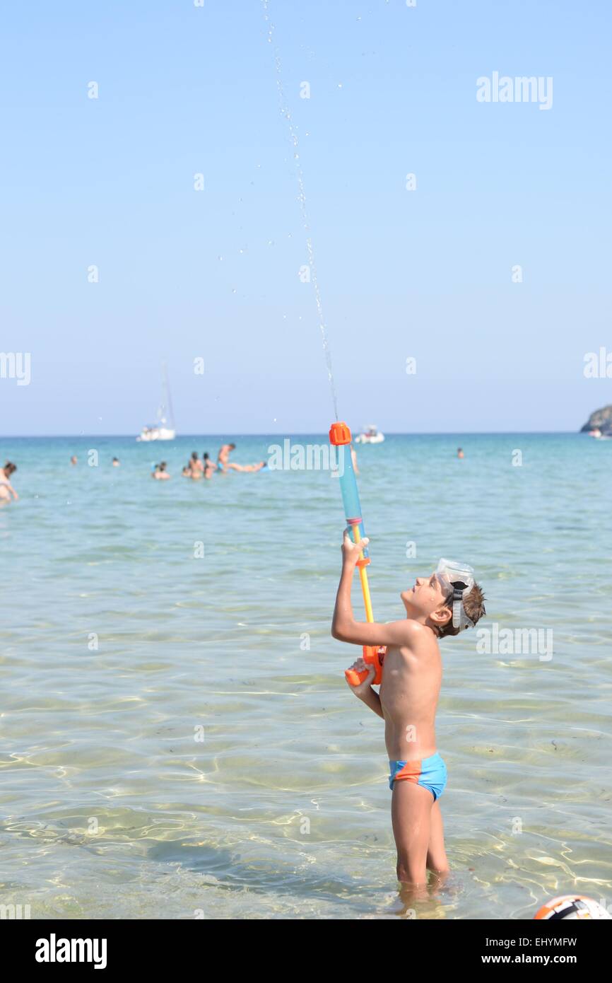 Boy standing in the sea playing with a water gun, Thassos, Greece Stock Photo
