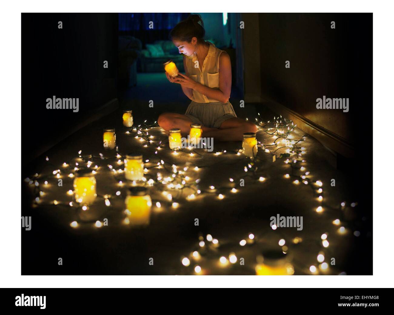 Young woman sitting on floor surrounded by fairy lights and tea lights Stock Photo