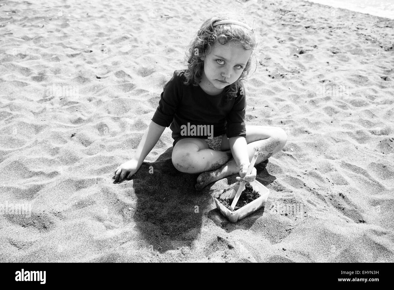 Sad looking girl sitting on the beach playing with sand, Italy Stock Photo